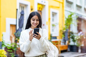 A young Indian girl walks on the city street and uses a mobile phone, calls, waits for an...