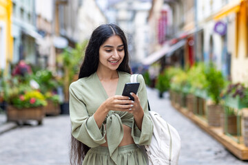 Smiling Indian young woman using mobile phone while standing in the middle of a city street wearing...
