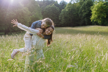 Two sisters playing at meadow in grass, having fun, piggybacking each other. Sisterly love and...
