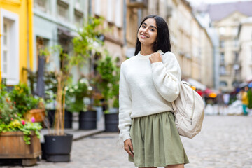 Indian young woman posing for camera, standing on city street with backpack and looking smiling