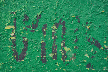 Peeling green paint on the concrete wall with old cracked flaking paint. Weathered rough painted surface with patterns of cracks and peeling texture for background                   