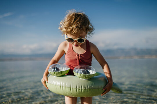Small girl at beach with inflatable toy ring, playing in water looking at sea.