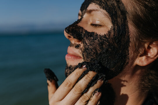 Woman applies healing mud to her face and body. Natural healing mud in Croatia on the beach.