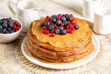 Stack of sweet homemade crepes, type of thin pancake, with blueberry and red currant. Breakfast on a white table.
