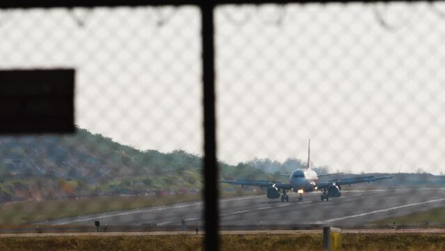 Airplane with an unrecognizable livery braking after landing. Flight arriving. View of the runway through the airport fence. Spoilers up