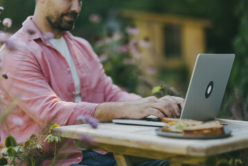 Man working outdoors in the garden, eating lunch, sandwich. Businessman working remotely from...