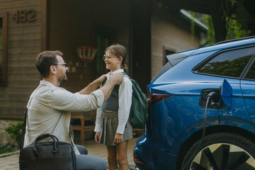 Portrait of a man charging electric car in front of his house.Man is unplugging charger from the fully charged car before driving daughter to school.