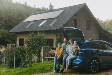 Family with electric car standing in front their house with solar panels on roof. Solar energy and sustainable lifestyle of young family. Concept of green energy and sustainable future for next - obrazy, fototapety, plakaty