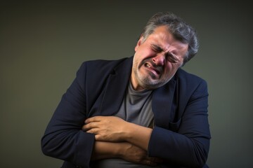 Obraz premium Photography of a man in his 50s clutching his stomach with a grimace of pain, against a solid taupe background, illustrating the discomfort of his abdominal distress