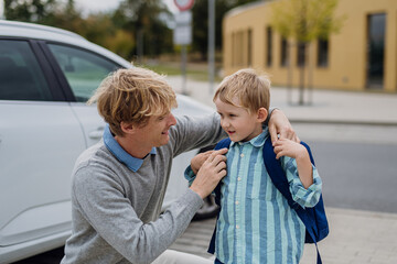 Father saying goodbyeto to son in front of school building, hugging him and helping with backpack. Dad heading to work. Concept of work-life balance for parents.