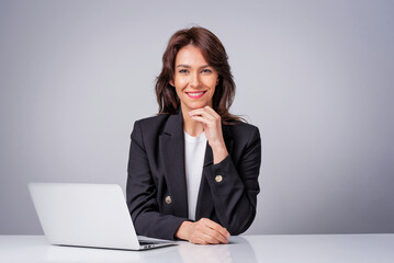 Studio shot of an attractive mid aged woman sitting at desk and using laptop against isolated white background