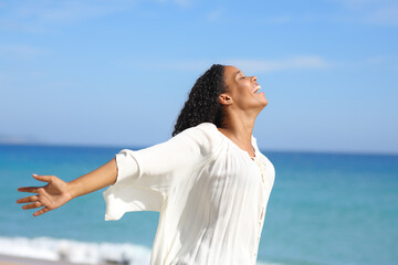 Happy black woman outstretching arms on the beach
