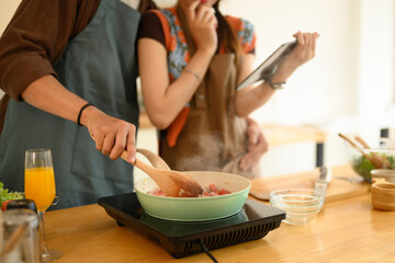 Young couple cooking together in the kitchen, man using a spatula stirs minced pork and garlic in a pan