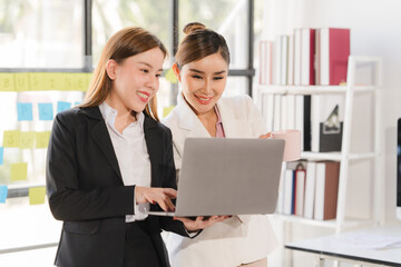 Two focused young Asian businesswomen or female accountants are discussing work, examining...