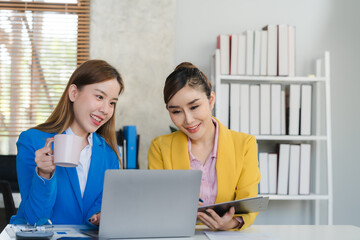 Two focused young Asian businesswomen or female accountants are discussing work, examining...