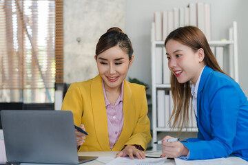 Two focused young Asian businesswomen or female accountants are discussing work, examining financial data, and working on reports in the office together.