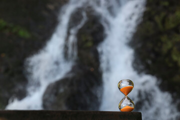 An hourglass with blur waterfall in background. fallen orange sand.