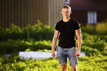 Horizontal knee length portrait of white man in her 20s, Caucasian male standing in garden at sunset