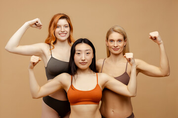 Group strong attractive multiracial women wearing colorful lingerie showing biceps isolated on background. Beautiful females  looking at camera. Diversity, feminism, International women's Day concept