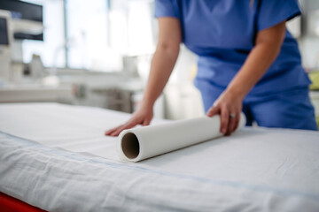 Nurse preparing examination table in emergency room, examination room. Discarding of used paper and rolling out the fresh sheet of paper for next patient. - obrazy, fototapety, plakaty