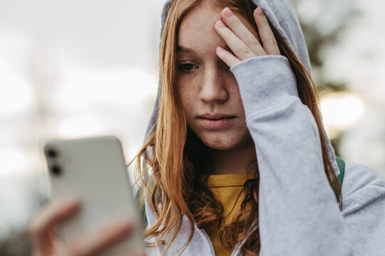 Portrait of teenage girl looking at her smartphone, sad, anxious, alone. Cyberbullying, girl is harassed, threated online.