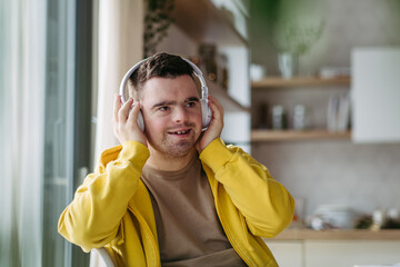 Young man with down syndrome listening his music via headphones. Sitting in kitchen, wireless...
