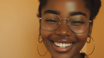 Smiling woman with glasses and hoop earrings against a warm yellow background.