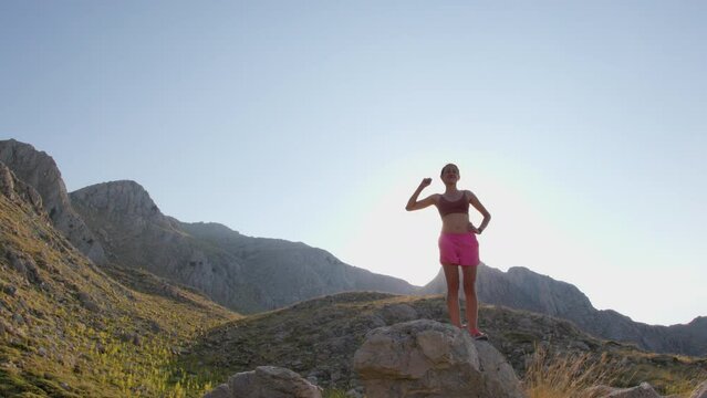 young woman has climbed to the top of a mountain and joyfully raises her hand up, traveling through the mountains, achieving success in achieving her goal. running in the mountains.