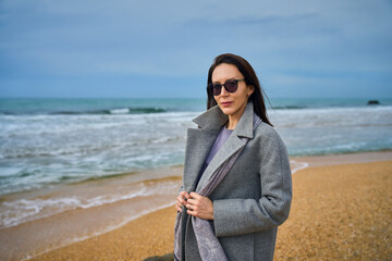 woman in warm clothes walks on a sandy beach by the sea