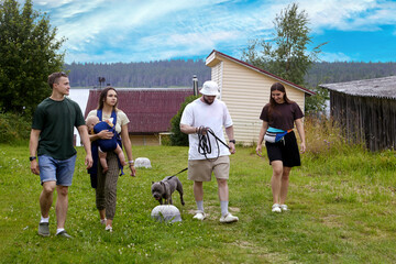 Two married couples are walking through village, one couple with baby in baby carrier, other couple with dog on leash.