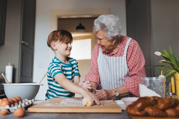 Grandmother with grandson preparing traditional easter meals, kneading dough for easter cross buns. Passing down family recipes, custom and stories.