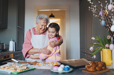 Grandmother with grandaughter preparing traditional easter meals, baking cakes and sweets. Passing...