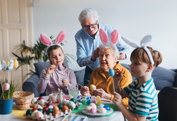 Grandmother with little kids decorating easter eggs at home. Tradition of painting eggs with brush...