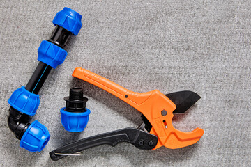 Ratcheting pipe cutter with fittings for HDPE pipes with an angle, coupling and threaded adapter equipped with compression clamp with collet, lie on gray surface.