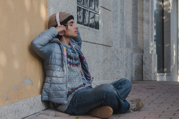 young man sitting relaxed with headphones on the street