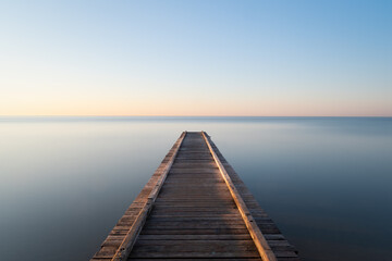 mystical photo of a rustic pier leading into a calm sea at sunrise - Powered by Adobe
