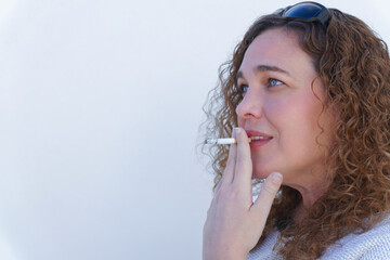attractive blue-eyed, curly-haired woman in profile smoking a cigarette with white background and...