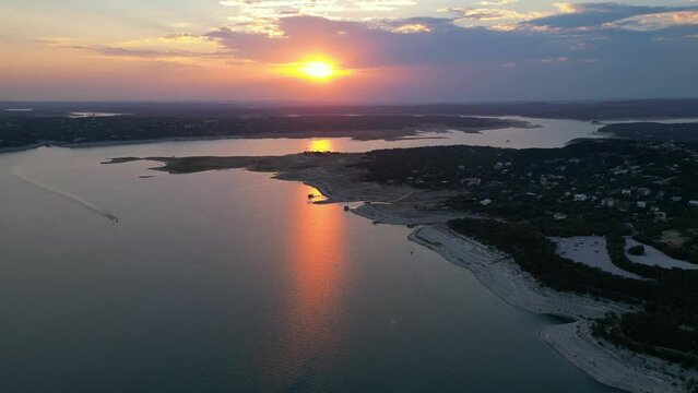 A boat speeding across Lake Travis as a fiery sunset is reflected on the water