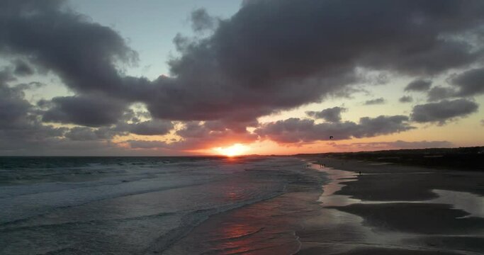 Sunset at the beach with dramatic clouds reflecting the warm glow of the sun, waves gently lapping the shore