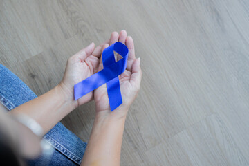Top view of woman sit on wooden floor and holding blue ribbon, Colon cancer awareness concept.