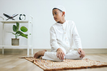Muslim kid wearing skullcap praying salat in sitting position, reciting the salam facing the right...