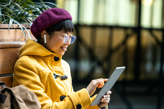 Beautiful Japanese woman in trendy coat using digital tablet in city street.