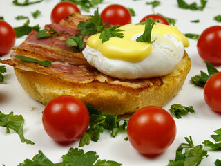Fototapeta na wymiar Egg Benedict with fried bacon placed on a plate with fresh cherry tomatoes, traditional breakfast 