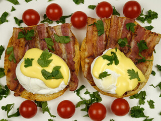 Eggs Benedict with fried bacon placed on a plate with fresh cherry tomatoes, traditional breakfast