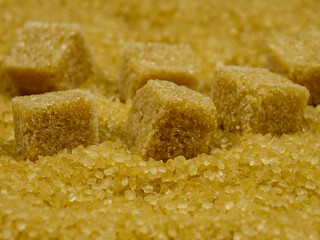 Brown sugar cubes lays on a brown granulated sugar, background 