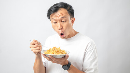 Portrait of an Indonesian Asian man, wearing a white T-shirt, enjoying eating noodles, isolated against a white background.