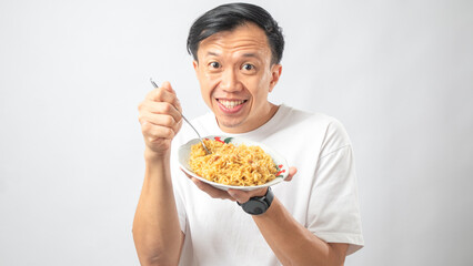 Portrait of an Indonesian Asian man, wearing a white T-shirt, enjoying eating noodles, isolated against a white background.