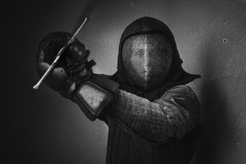 Portrait of a man dressed in black historical fencing armor and fencing protective helmet mask with...