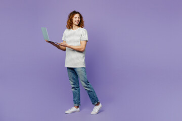 Fototapeta premium Full body smart fun young IT man he wears grey striped t-shirt casual clothes hold use work on laptop pc computer isolated on plain pastel light purple background studio portrait. Lifestyle concept.