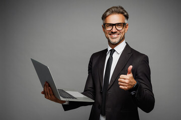 Side view happy adult employee IT business man corporate lawyer he wears classic formal black suit shirt tie work in office hold use laptop pc computer show thumb up isolated on plain grey background.